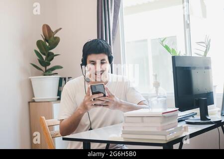 Asian man administrator staff call center in home service office assistance work from home looking data customer from computer communication during co Stock Photo