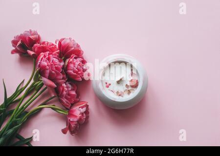 Ecological and vegan handmade candle with dry flowers in a glass made of concrete on a pink background with pink tulips. Soy or coconut candle with a wooden wick. Stock Photo