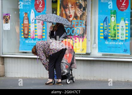 Dundee, Tayside, Scotland, UK. 6th July, 2021. UK Weather: A cloudy and wet day with outbreaks of light rain across North East Scotland with temperatures reaching 17°C. Local residents are still well aware of the social distancing guidelines and the wearing of face masks whilst outside. Shoppers who are caught out in the sudden downpours are sheltering underneath their brollies whilst out shopping in Dundee city centre. Credit: Dundee Photographics/Alamy Live News Stock Photo