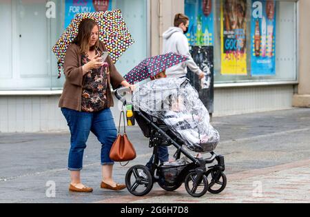 Dundee, Tayside, Scotland, UK. 6th July, 2021. UK Weather: A cloudy and wet day with outbreaks of light rain across North East Scotland with temperatures reaching 17°C. Local residents are still well aware of the social distancing guidelines and the wearing of face masks whilst outside. Shoppers who are caught out in the sudden downpours are sheltering underneath their brollies whilst out shopping in Dundee city centre. Credit: Dundee Photographics/Alamy Live News Stock Photo