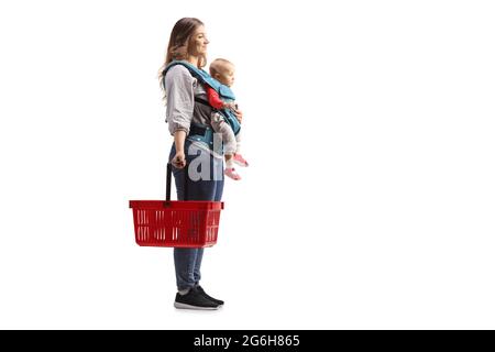 Full length profile shot of a mother with a baby in a carrier holding a shopping basket isolated on white background Stock Photo