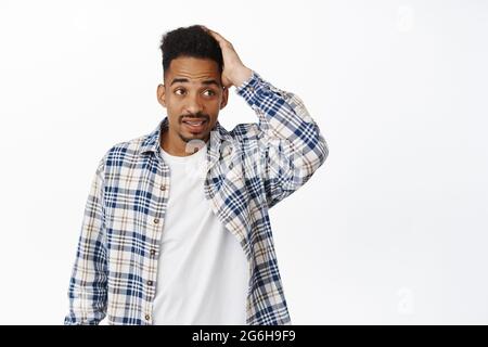 Young puzzled and confused african american guy dont know what to do, scratch head and look aside with questioned clueless face, dont understand whats Stock Photo
