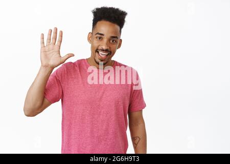 High five. Smiling african american guy raising hand up, waving hello with friendly face expression, greeting, make hi gesture, standing in pink t Stock Photo