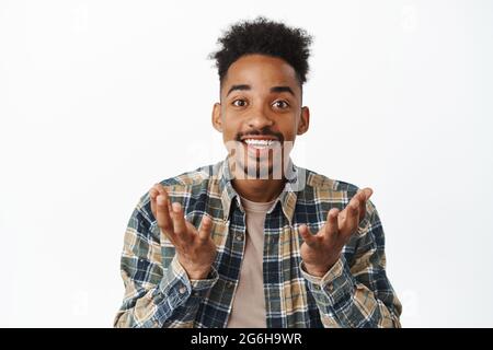 Close up portrait of happy african american man looking surprised and proud of you, raising hands as if holding smth in empty palms, making Stock Photo