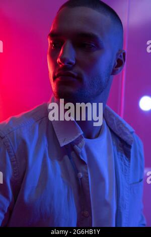 Cinematic portrait of handsome young man in neon blue pink lighted room, stylish male model indoors. Reflection effect Stock Photo