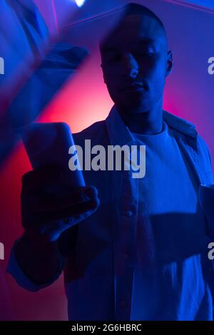 Cinematic portrait of handsome young man in neon blue pink lighted room, stylish male model indoors. Reflection effect Stock Photo