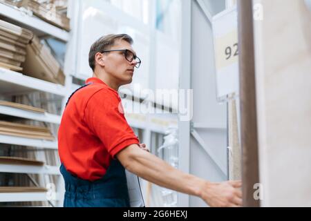 employee of a flooring store standing near the shelves with a laminated board. Stock Photo