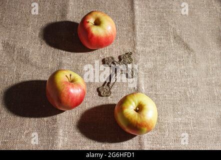 bronze cross and three red apples on the table. closeup on black background Stock Photo