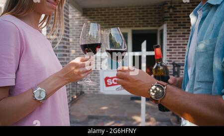 cropped view of couple clinking glasses of red wine near new house