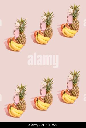Creative pattern made of fresh bananas, pineapple, pomegranate and refreshment juice in glass on pastel pink background. Natural green plant shadow. S Stock Photo