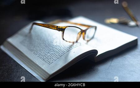 A pair of reading glasses resting on an open book.