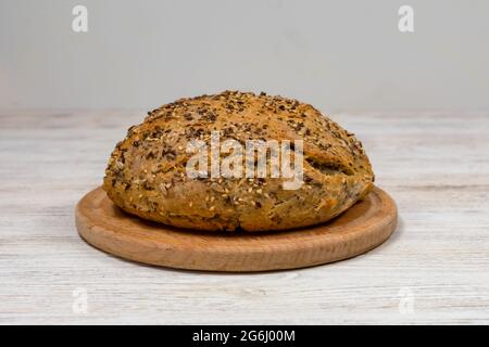 Natural loaf of yeast-free sourdough bread with sesame seeds, flax, chia, sunflower seeds, on a wooden board on the table, close-up. Stock Photo