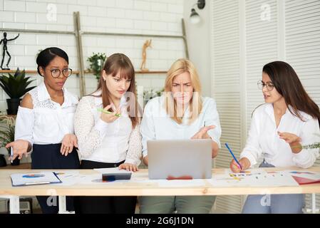 Serious female multiracial team solving problem together, diverse focused african, asian and caucasian colleagues discuss project brainstorming workin Stock Photo