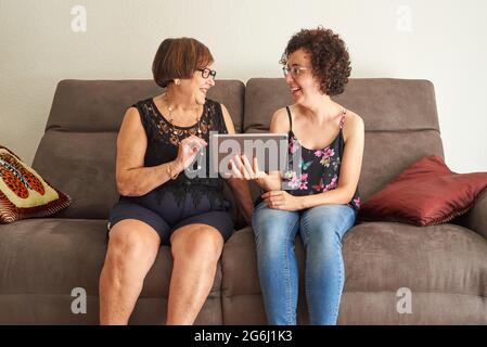 Grandmother and granddaughter laugh while watching digital content on tablet Stock Photo