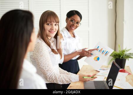 Smiling women work together in a modern office. Feminism. Professional smiling business women standing in the office and discussing business papers. Stock Photo