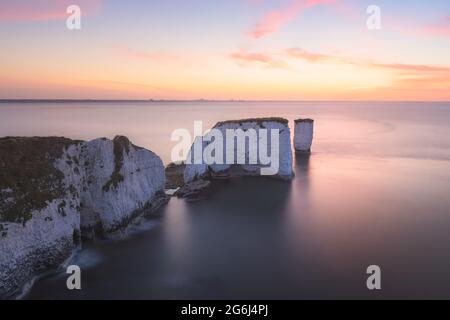 Colourful, idyllic sunset or sunrise sky over seascape landscape of the white chalk cliffs and sea stacks of Old Harry Rocks on the Jurassic Coast in