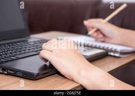 Closeup a woman hand using a laptop computer working at her desk in the office. A businesswoman is writing down her work in a notebook. work from home Stock Photo