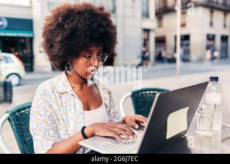 afro woman sitting on a bar terrace and using a laptop. Concept of working on remote from a cafeteria Stock Photo