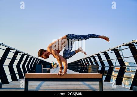 Fit man doing a hand stand while practicing yoga alone near the ocean against sky at dusk or dawn Stock Photo