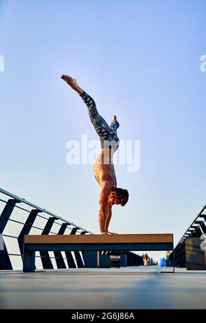 Fit man doing a hand stand while practicing yoga alone near the ocean against sky at dusk or dawn Stock Photo
