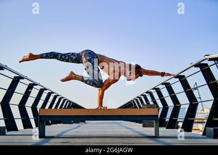 Fit man doing a hand stand while practicing yoga alone near the ocean against sky at dusk or dawn Stock Photo