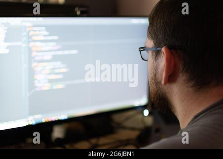 An over the shoulder view of a software engineer in a home environment debugging code. The engineer has a beard and glasses. Stock Photo