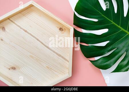 Tropical green palm leaf and empty wooden tray on a pink background. Monstera leaves mockup, template. Summer fashion background. Stock Photo