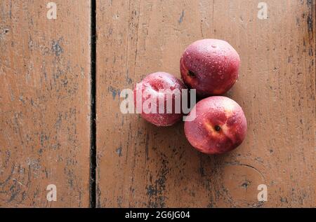 Three peaches on a wooden table. Juicy red fruits lie on a red wooden surface. Stock Photo