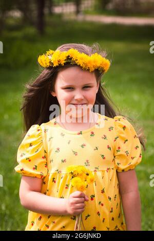 vivid sunny portrait of a five-year-old girl with a wreath and a bouquet of dandelions, a dandelion as a symbol of summer and the sun Stock Photo