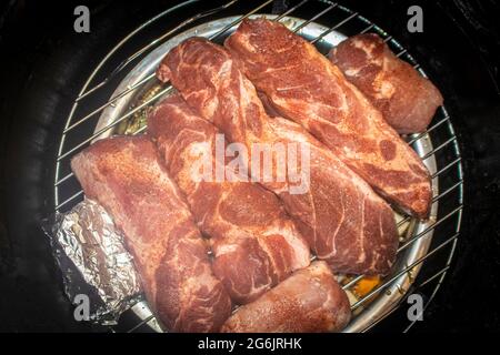 Raw seasoned pork ribs on grill inside barrel food smoker with herbs in tin foil to side Stock Photo