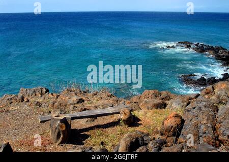 Horizon stretches out in deep blue aqua along the rocky stretch of shoreline at Lapakahi State Historical Park.  A single rustic log-hewn bench sits o Stock Photo