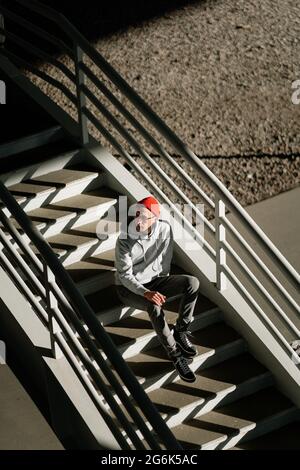 Lonely young man in glasses sit alone on concrete stairs in urban building or city space, above view Stock Photo