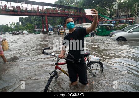 A man takes selfies in rain water on the streets during the monsoon rain. Couple of hours of rain create waterlogging on the streets as the sewerage and drains system is not cleared and maintained properly. Dhaka, Bangladesh. Stock Photo