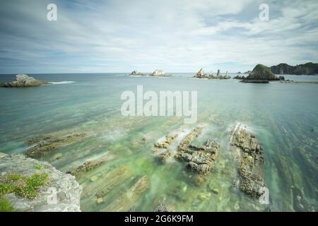 Sharp intertidal rock ridges at Playa de Gueirúa in Asturias, Spain, showing layered geology beneath clear Atlantic waters on a calm coastal day Stock Photo