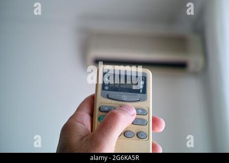 Closeup of a hand with air conditioner remote setting comfortable temperature in a room Stock Photo
