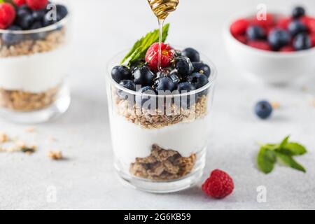 Honey is poured on granola with yogurt, blueberries and raspberries. Healthy breakfast. Menu, recipe. Stock Photo