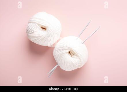 White knitting wool and knitting needles on pastel pink background. Hobby knitting. Top view - Image Stock Photo