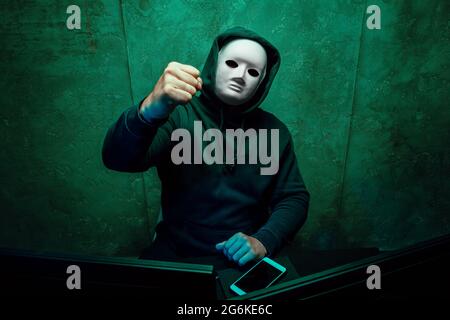 Anonymous hacker wearing face mask working on computer in dark room Stock Photo