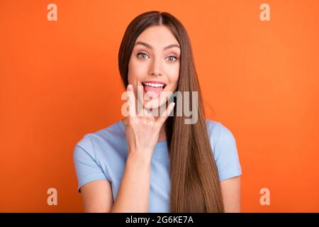 Photo of crazy brown hairdo millennial lady show rock sign tongue out wear blue t-shirt isolated on vivid orange color background Stock Photo