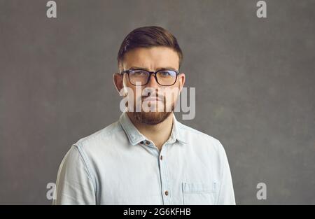 Close up studio portrait of millennial man with serious facial expression on gray background. Stock Photo