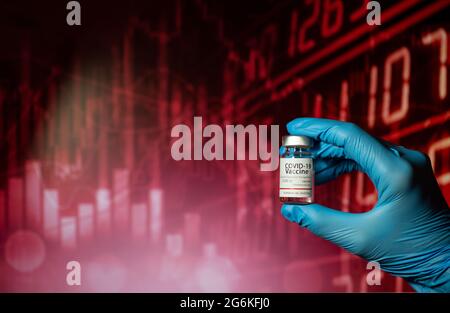 Hands of a researcher in medical gloves holding a Coronavirus Vaccine  with stock index chart background. Stock Photo