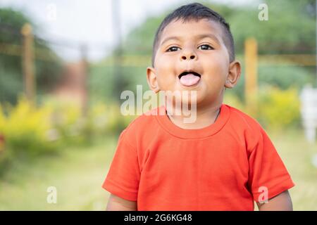 Portrait of Cute little Indian toddler grimacing by making tongue out while playing at park with copy space Stock Photo