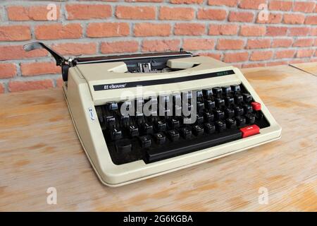An old typewriter. A typewriter located on the wooden table. There is a brick wall in the background. Stock Photo