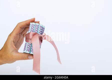Ukrainian money wrapped with a gift ribbon in a hand. Stock Photo