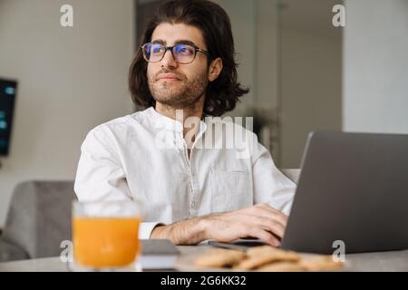 Mid aged brunette turkish man sitting at the table with laptop computer at home Stock Photo