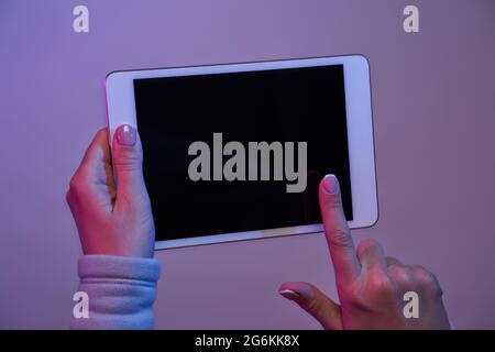 Close-up of hands with tablet and blank black screen on blank purple background. Stock Photo