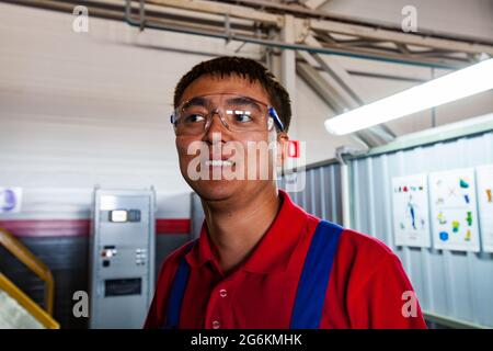 Atyrau, Kazakhstan - May 21,2012: Flowserve company plant. Portrait of young Asian worker in protective glasses, blue coveralls and red polo shirt. Wh Stock Photo