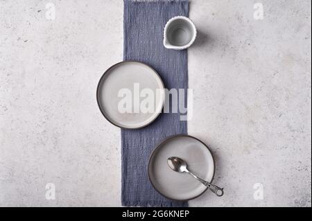 Empty light plates with saucer, spoon and napkin set on gray graphite textured background. Top view, copy space Stock Photo