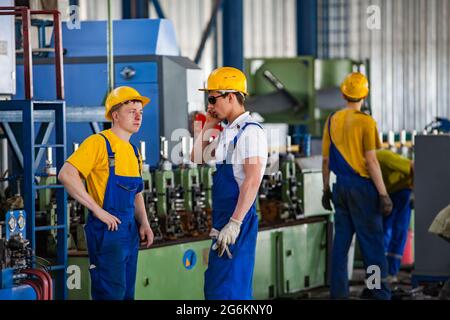 Almaty region,Kazakhstan-June 06,2012: Three workers in yellow t-shirts and hardhats and blue overalls in SONiK factory workshop. Metalworks machine o Stock Photo