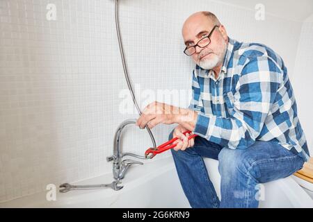 Plumber or caretaker with pipe wrench assembles the shower's shower hose Stock Photo